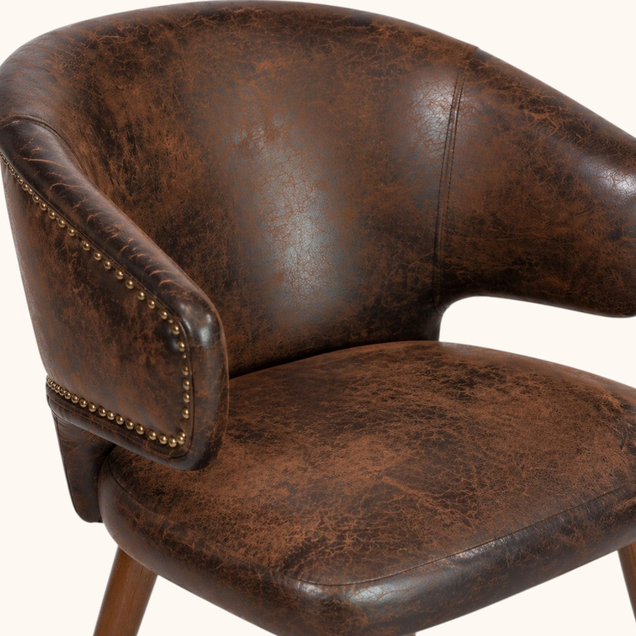 Stuhl mit brauner Polsterung in Used-Leder-Optik, gerundeter Rückenlehne, integrierten Armlehnen, Ziernieten, Holzbeinen und metallfarbenen Fußkappen, stilvoller Designerstuhl