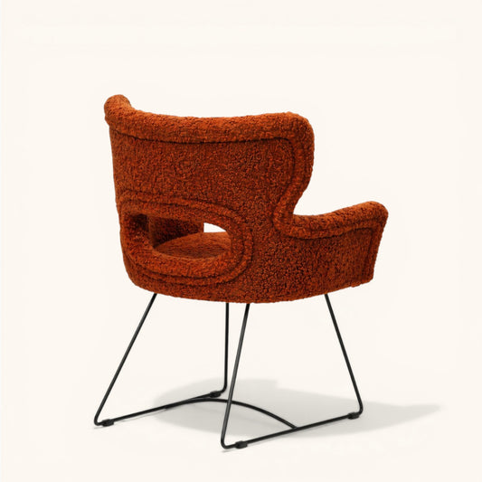 Stuhl mit orangefarbenem Bouclé-Bezug, gerundeter Rückenlehne mit offener Aussparung, integrierten Armlehnen und schwarzem Metallgestell, moderner Designerstuhl