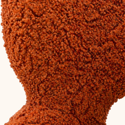 Stuhl mit orangefarbenem Bouclé-Bezug, gerundeter Rückenlehne mit offener Aussparung, integrierten Armlehnen und schwarzem Metallgestell, moderner Designerstuhl