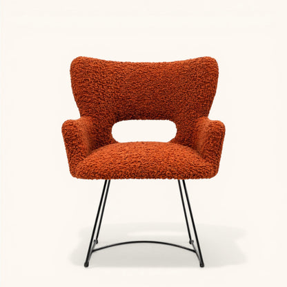 Stuhl mit orangefarbenem Bouclé-Bezug, gerundeter Rückenlehne mit offener Aussparung, integrierten Armlehnen und schwarzem Metallgestell, moderner Designerstuhl